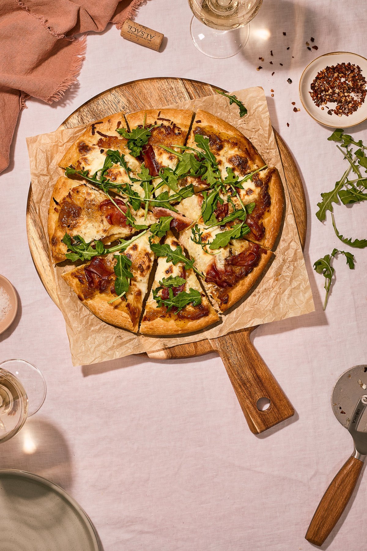 Artisanal prosciutto and arugula pizza on a wooden paddle with wine